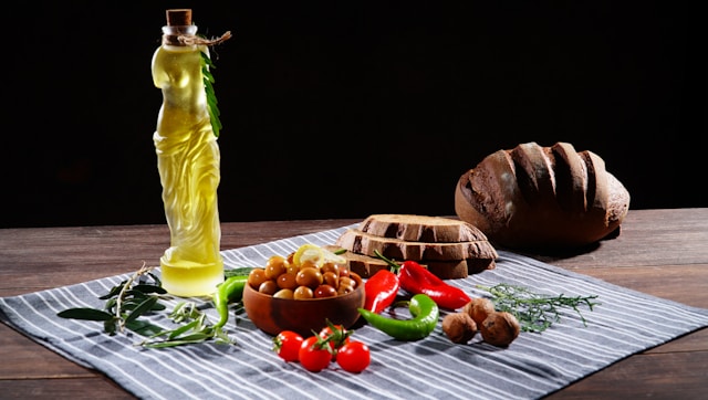 A rustic flat-lay of Mediterranean diet foods including olive oil, olives, fresh vegetables, grilled fish, lentils, whole grain bread and red wine, representing the evidence-based dietary pattern for longevity.