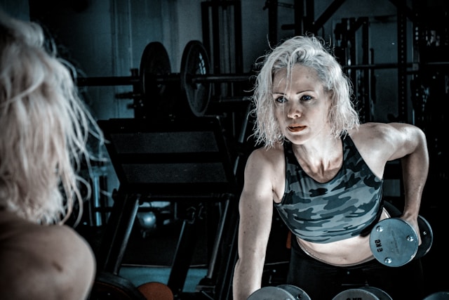 A fit woman in her 40s lifting a dumbbell in a gym, representing the shift away from excessive cardio toward strength training for midlife health.