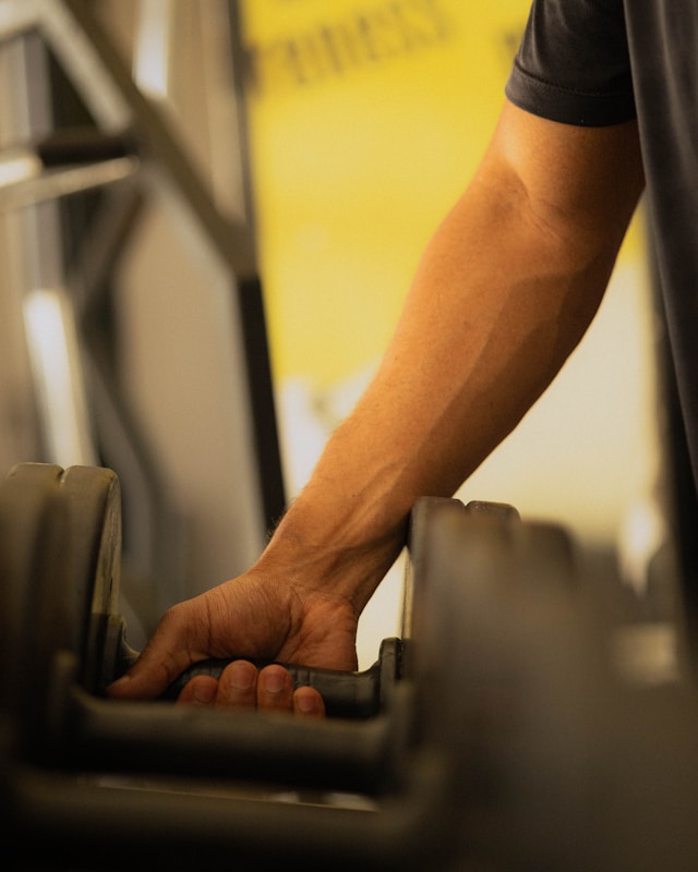 Hand reaching for a dumbbell in a gym for consistent strength training after 40.